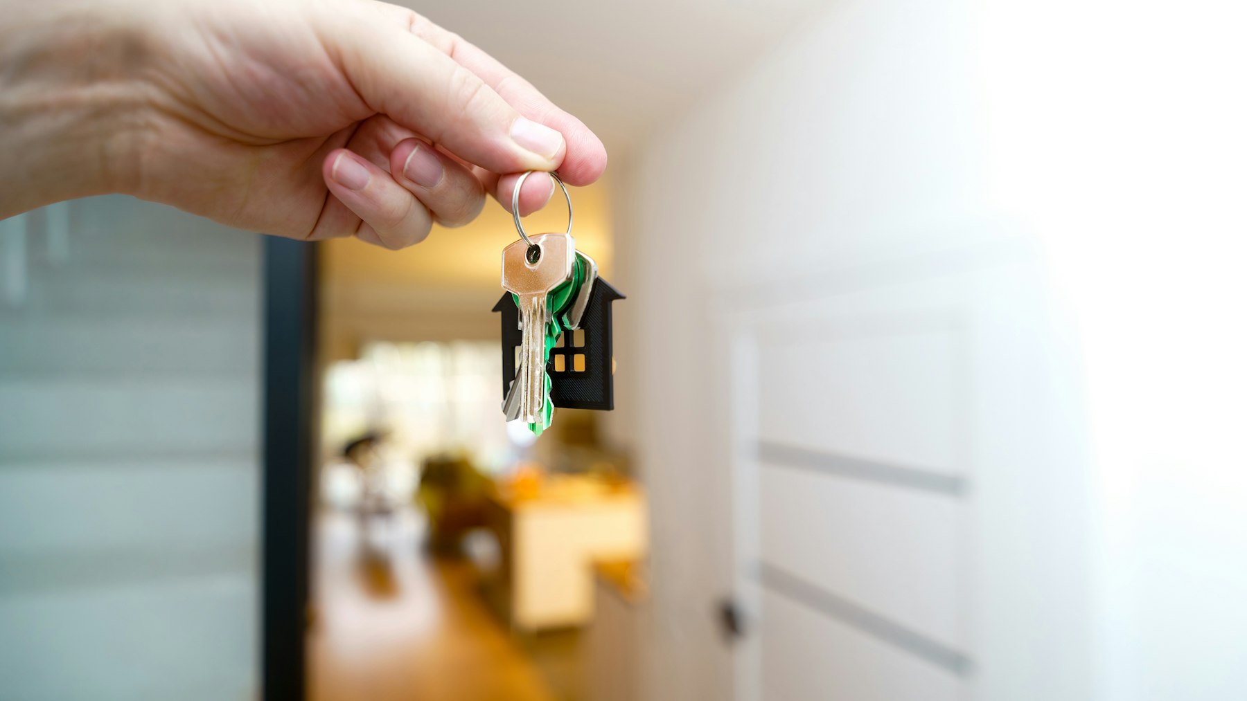 Hand holding house keys on a house-shaped keychain in a bright entryway